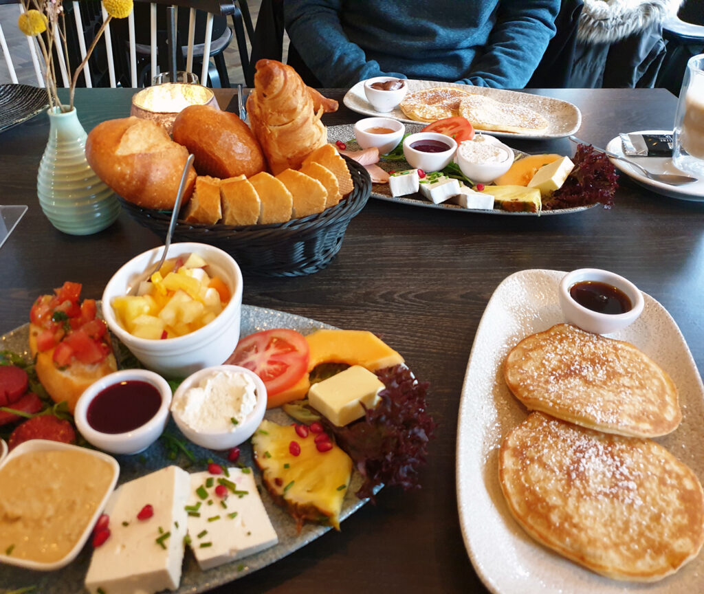 Den Zufall einladen: Frühstückstisch in einem Restaurant mit Pancakes, Brötchen und verschiedenen Aufstrichen.